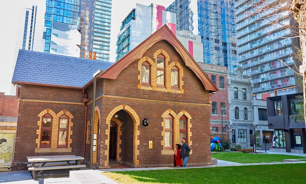 A couple walking into a tiny brick cottage in the city.
