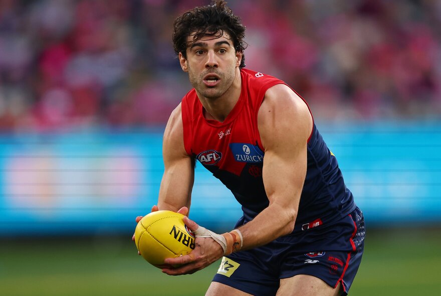 A Melbourne football player looks hurried as he tries to pass on the ball.