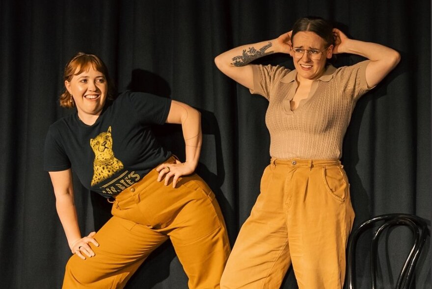 Two impro theatre performers interacting on a stage and striking exaggerated poses.