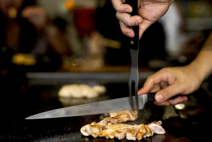 Chef carving meat on a hot plate.