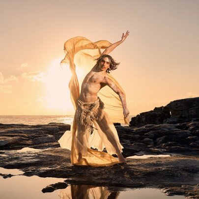 Indigenous dancer on a rocky foreshore at dawn waving a chiffon scarf.