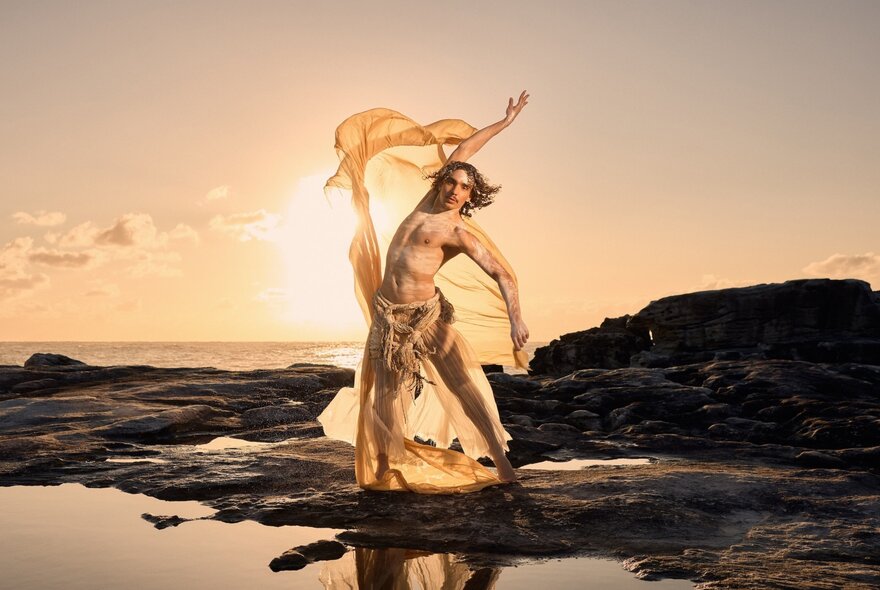 Indigenous dancer on a rocky foreshore at dawn waving a chiffon scarf.