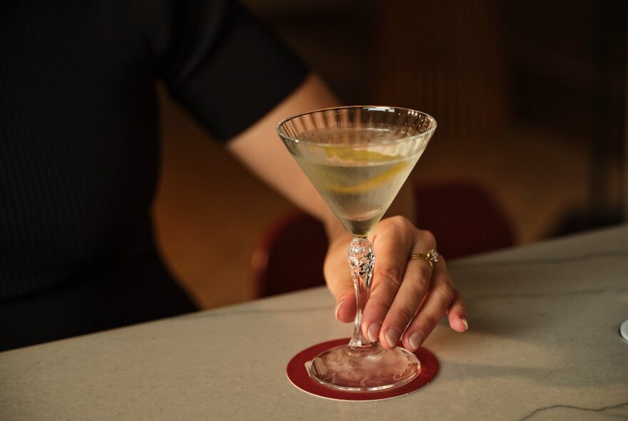 A hand on a Martini, the glass visibly cold. 