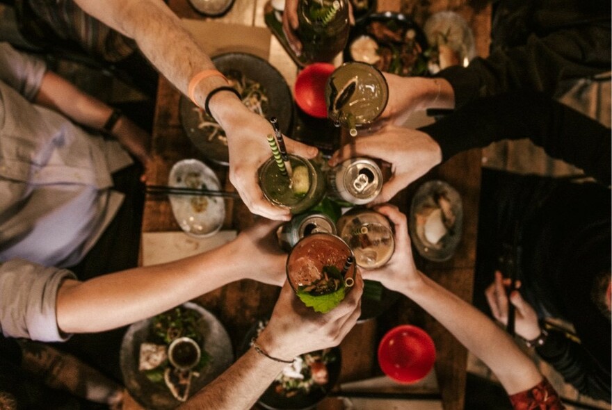 Many hands clinking glasses over a table of food.