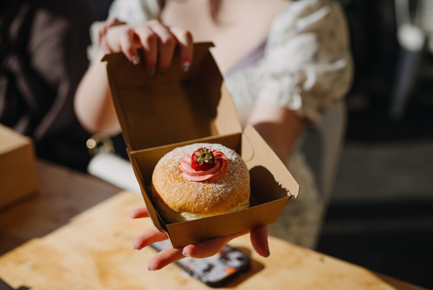 Hands of a person presenting a single donut in a box.