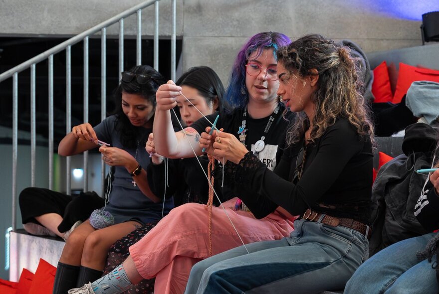 A group of four seated people crocheting together, interacting and talking. 