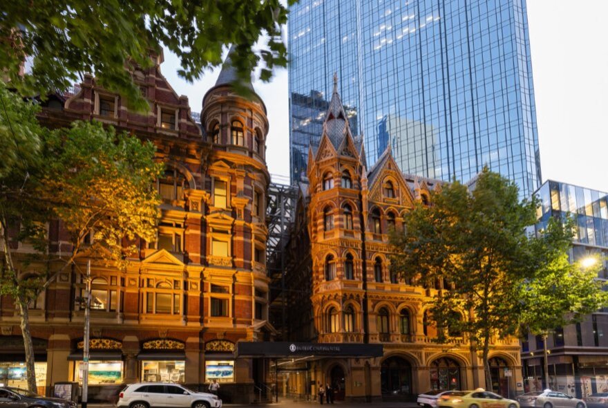 Exterior of InterContinental Melbourne The Rialto, featuring a distinct 1890s neo-gothic brick facade, with trees in the foreground and a tall skyscraper behind it.