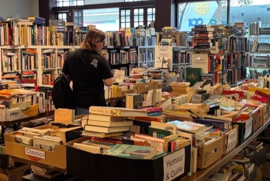 A person surrounded by shelves and boxes stacked with books in a used bookstore.