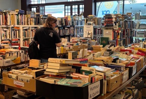 A person surrounded by shelves and boxes stacked with books in a used bookstore.