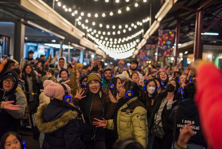 A very crowded market walkway at night with people in warm jackets and strings of lights overhead. 