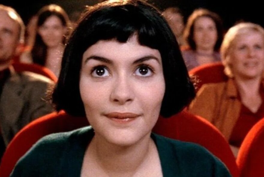 Audrey Tautou sitting in a movie theatre in a scene from the film Amelie.