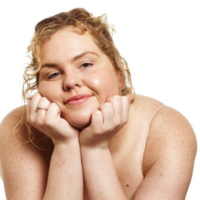 Comedian Tarsh Jago, leaning forward with their chin resting on their hands, smiling.
