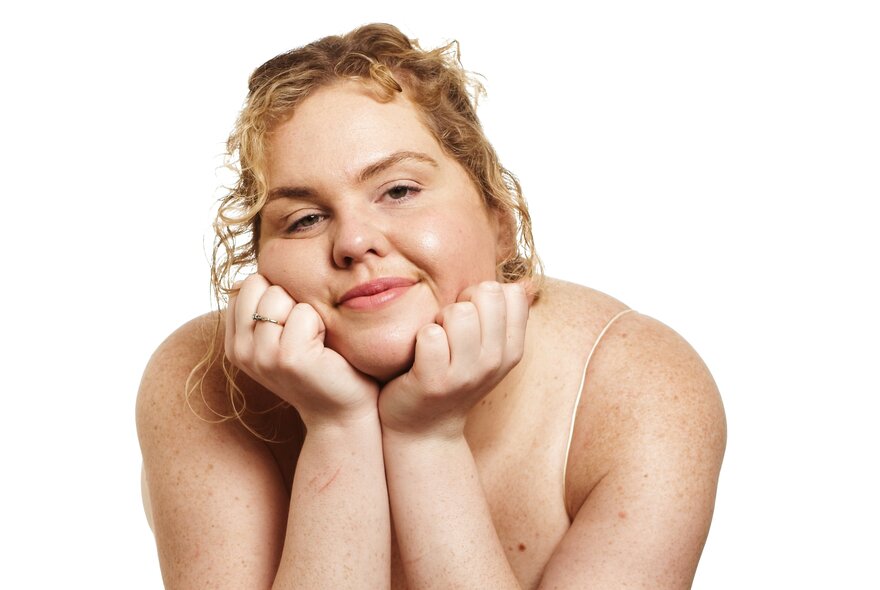 Comedian Tarsh Jago, leaning forward with their chin resting on their hands, smiling.
