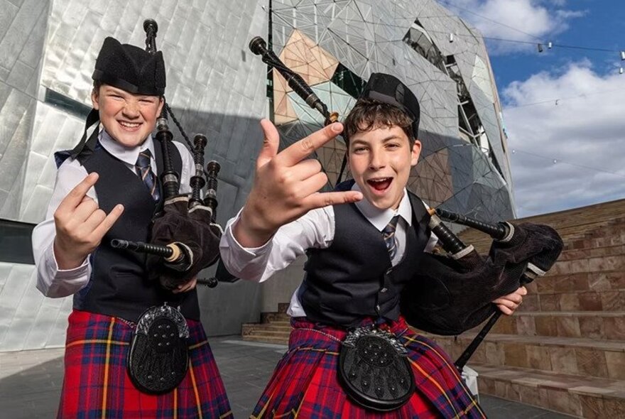Two young bagpipers dressed in traditional Scottish kilts in front of Fed Square in Melbourne.