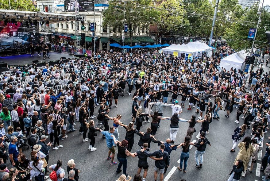 Aerial view of a large crowd of people in a city intersection that has been blocked for a street festival, watching dancers perform.