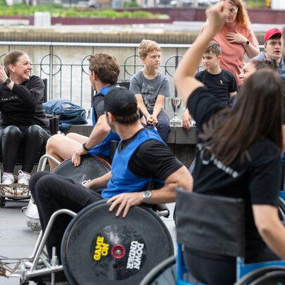 An outdoor area, with several people in wheelchairs engaged in a sporting activity, throwing a ball with their hands and wheeling around the area.