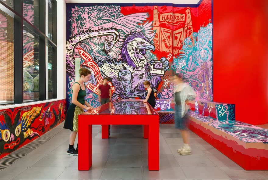 Blurred people around a large red table in a room with graffiti-like art on the red walls. 