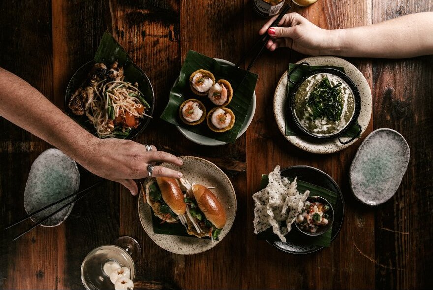 Hands reaching for a selection of Asian dishes and burgers. 