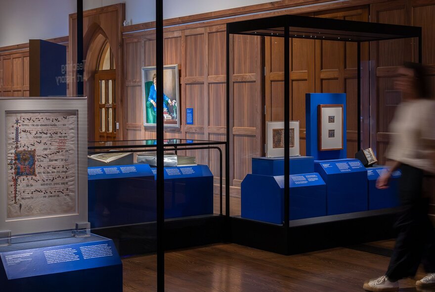 A gallery-like space with wooden wainscoting and framed medieval manuscripts displayed with blue information boards.
