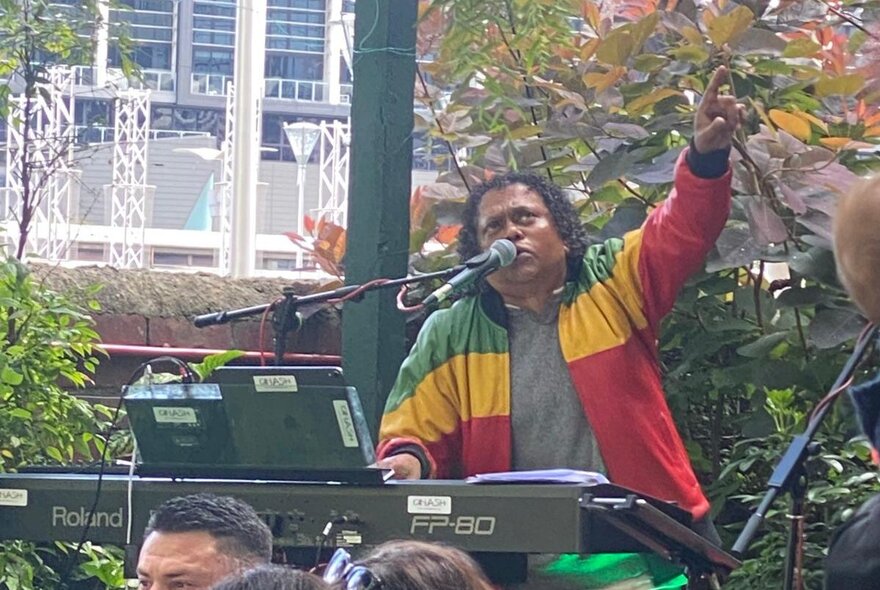 Soul musician Dinash Daniel playing the keyboard in an outdoor setting, wearing a red, yellow and green jacket.