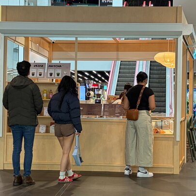 A timber booth in a shopping centre with people queuing for matcha drinks. 