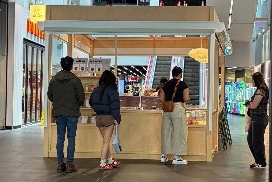 A timber booth in a shopping centre with people queuing for matcha drinks. 