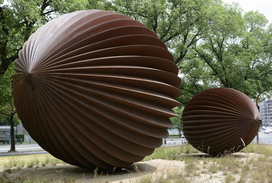 Two large pod-like steel sculptures in parkland.