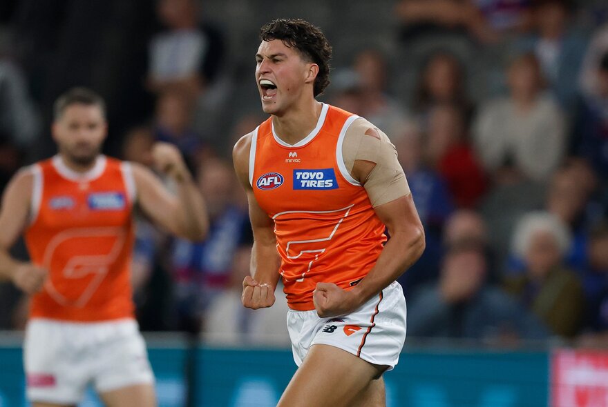 A GWS Giants AFL player cheering and looking happy with pumped fists, after scoring during a football match.