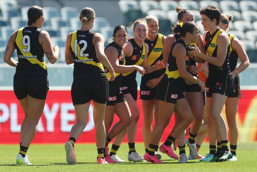 Richmond AFLW players celebrating on the field, coming together for a group huddle.