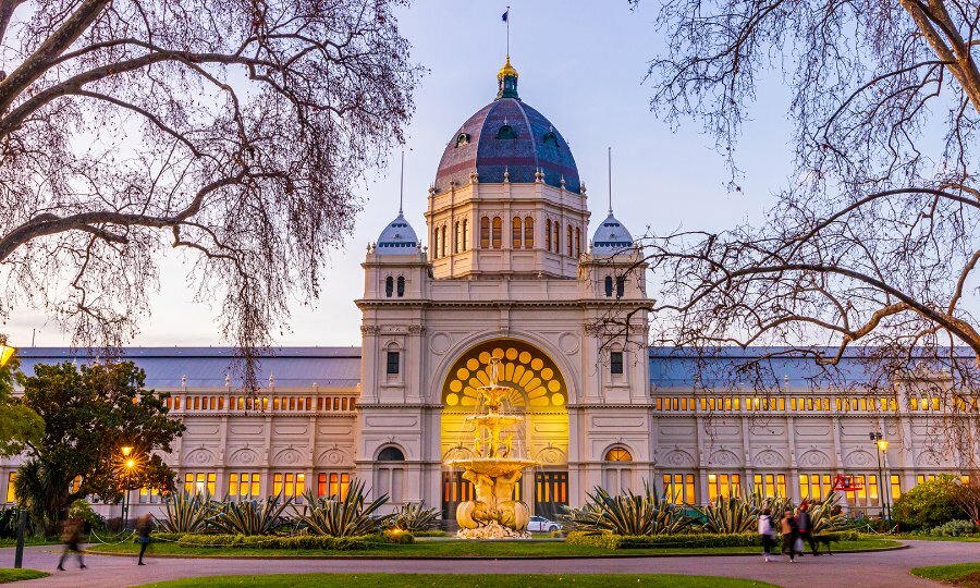 People walking past the Royal Exhibition Building with a fountain in front and a grand domed roof.
