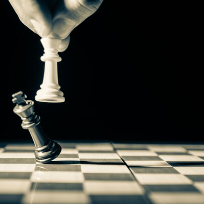 A hand holding a white chess piece, knocking over a black chess piece on a chessboard.