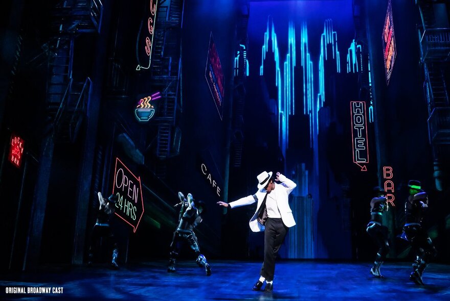 A dancer on stage in a white jacket and black pants, in the role of Michael Jackson, with a cityscape theatre backdrop behind them, in the stage production of MJ the Musical.