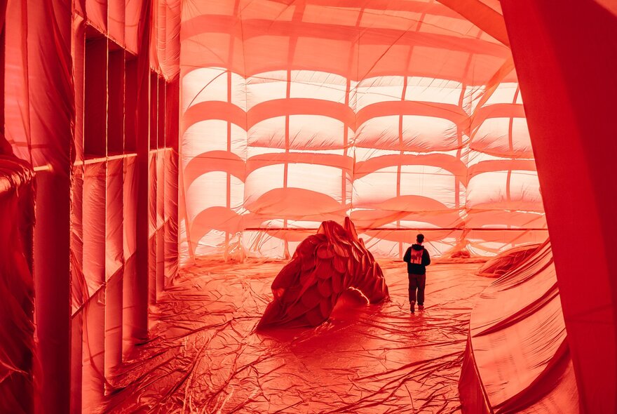 A person is standing in a building draped in a red fabric installation 
