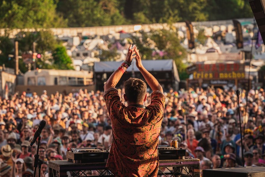 DJ Chris Arnold, seen from behind as he's on stage, performing to a large crowd of people at a festival.