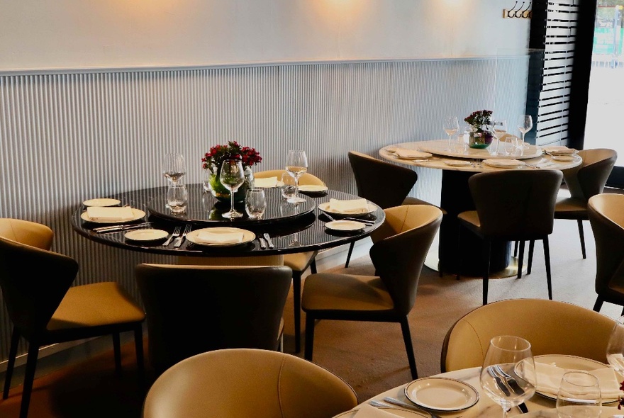 Restaurant interior with moody lighting, round tables set for dinner with rounded chairs.