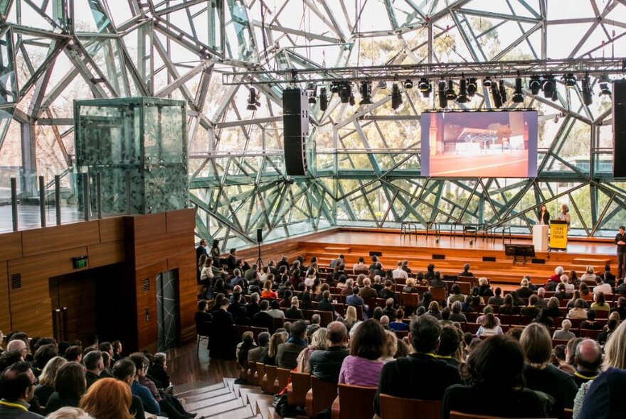 Inside The Edge at Federation Square with an elaborate design of glass and metal, an audience seated before an empty stage. 