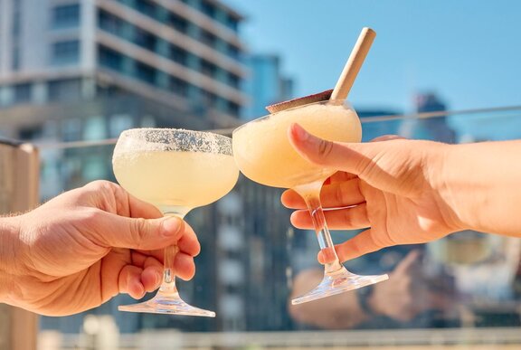 People clinking margarita glasses on a sunny rooftop.