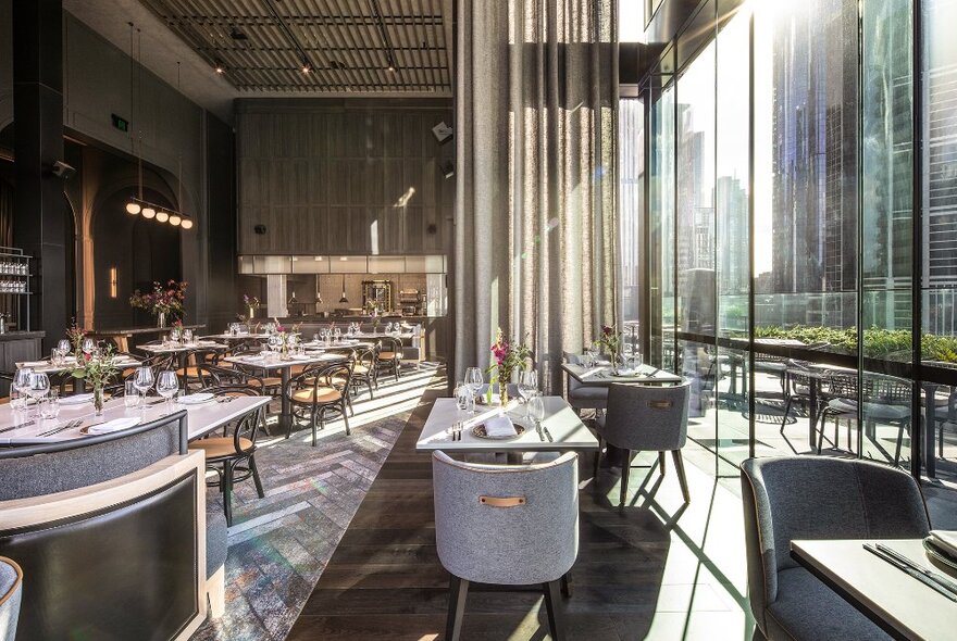 Sunshine pouring in through windows and drapes into a restaurant with white tables and chairs.