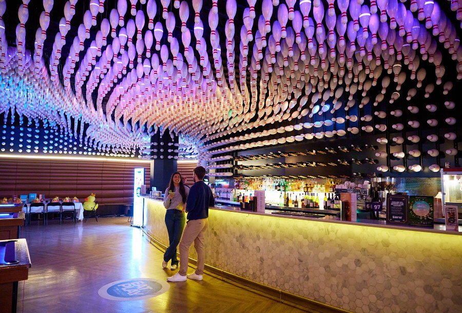 A couple standing at a bar under a ceiling covered in bowling pins.