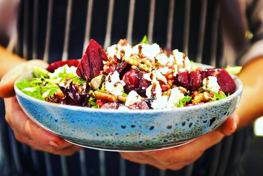 Waiter's hands holding a blue bowl filled with salad.