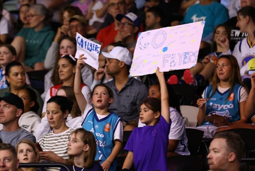 Sports fans holding signs, seated in tiered stadium.
