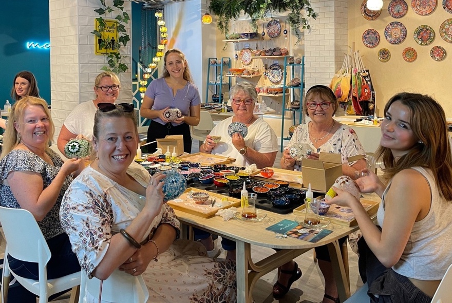 People seated at a table holding their completed Turkish mosaic lamps, smiling.