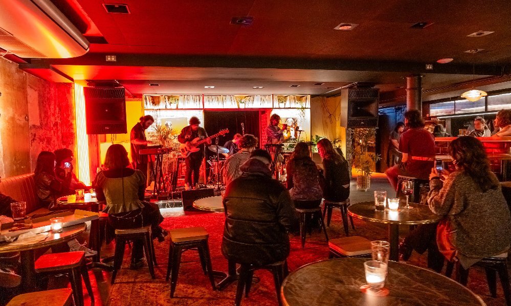 Inside a dimly-lit bar with people watching a live band on stage.