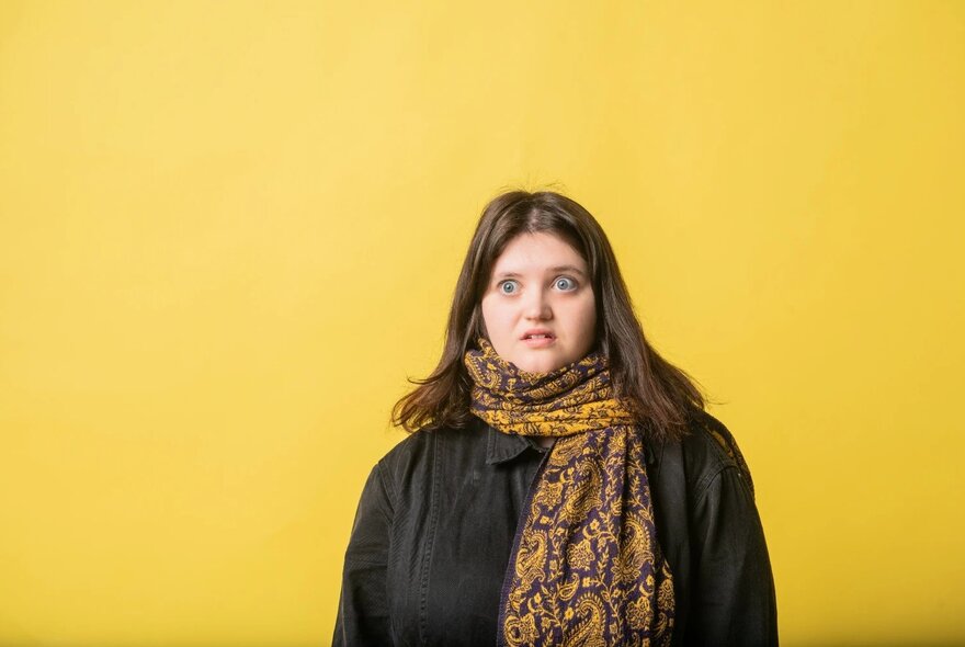Woman wearing a winter scarf and jumper, looking surprised.