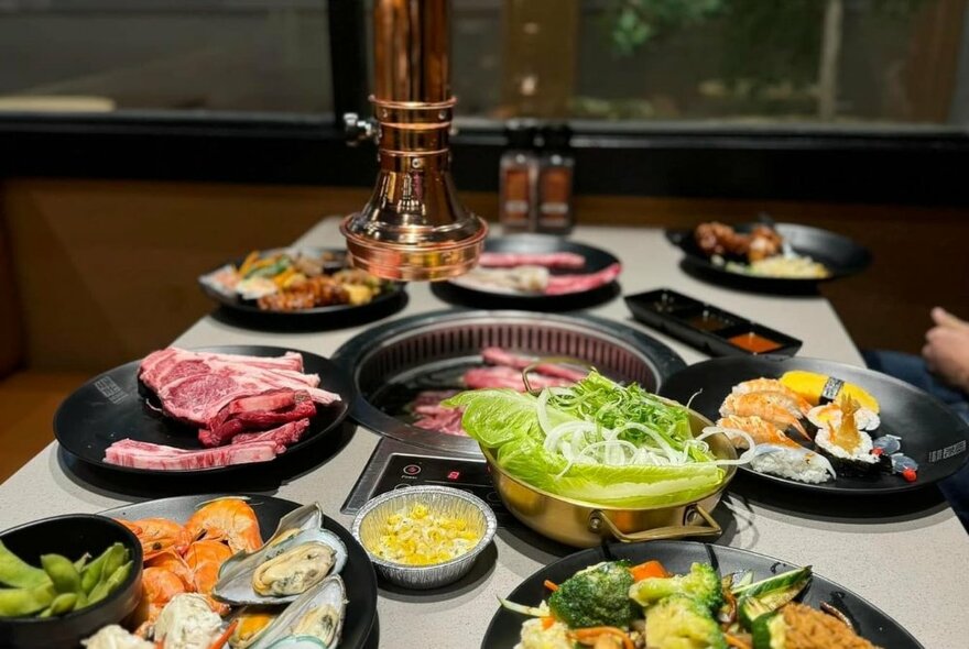 A restaurant table set with a central grill for cooking meat surrounded by plates of meat and vegetables.