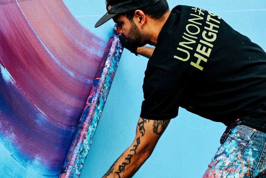 Sahil Roy painting a blue toned mural in a t-shirt that says Union Heights. 