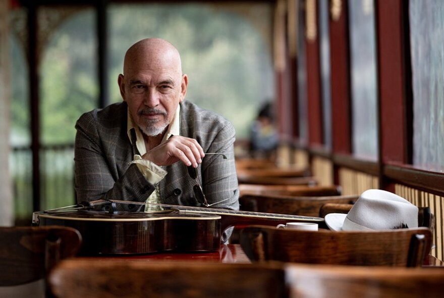 Musician Joe Camilleri seated at a table with his guitar and hat.