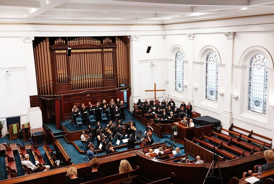 Choir in front of pipe organ in white Baptist church interior with wooden pews.