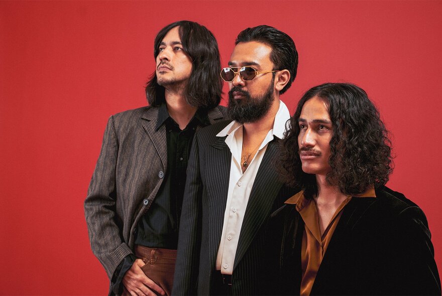 Three men in a line, looking at something above them, all wearing suits.