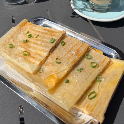 A high-angle shot of several pieces of golden-brown, folded flatbread garnished with sliced spring onion greens, served on a rectangular metal tray on a dark outdoor table.